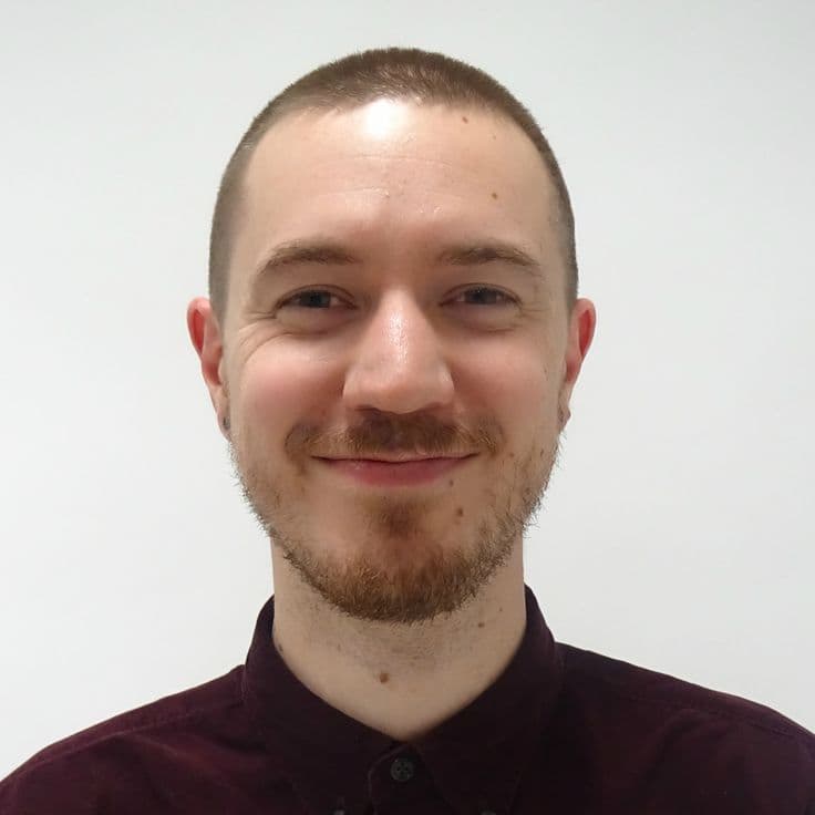 Smiling man with short hair and a beard wearing a dark maroon button-down shirt.